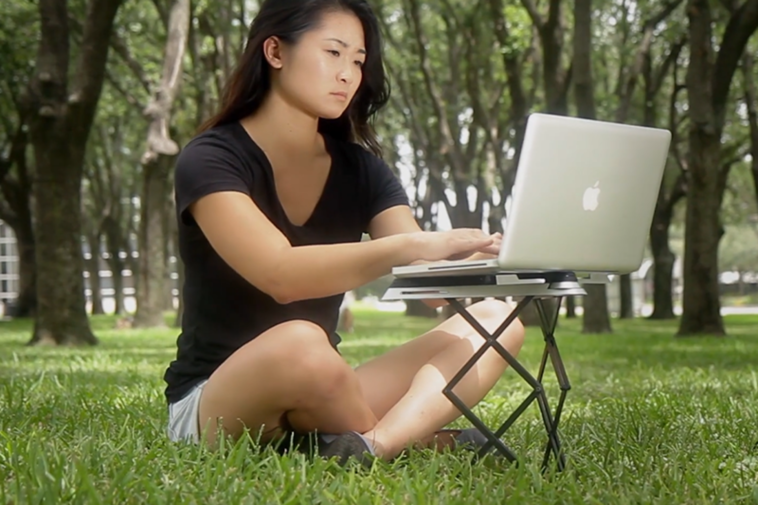 A woman working on a laptop in a park using a laptop stand