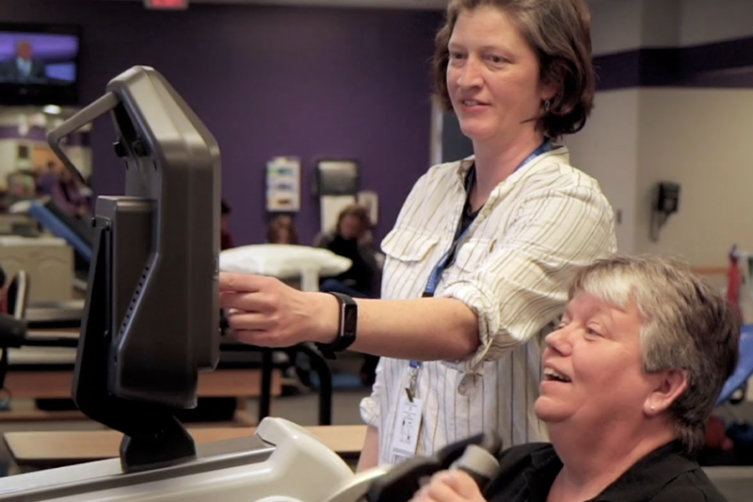 A woman helping another woman on a piece of rehabilitation equipment in a corporate video